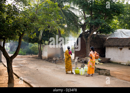 Le donne indiane il riempimento di bicchieri in plastica con acqua da un tubo montante in un territorio rurale villaggio indiano street. Andhra Pradesh, India Foto Stock