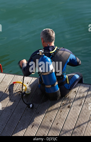 Scuba Diver sat sul pontile a Weymouth preparando per tuffarsi nel novembre Foto Stock