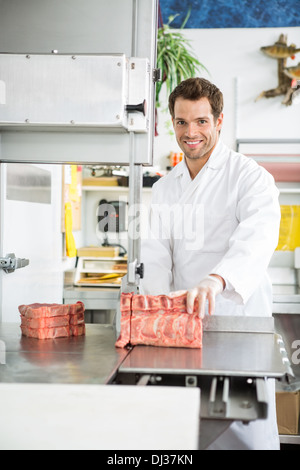 Ritratto di macellaio il taglio di carne a fette sulla segatrice a nastro Foto Stock