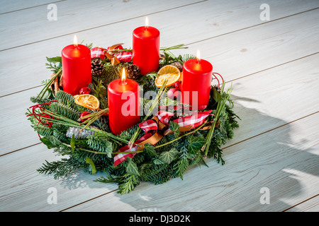 Corona di avvento di ramoscelli con la masterizzazione di quattro candele rosse e ornamenti vari Foto Stock
