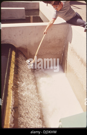 Un tecnico raccoglie un campione di acqua dall'uscita di un impianto di trattamento delle acque reflue, un processo essenziale per monitorare la qualità dell'acqua e garantire la sicurezza ambientale nella gestione delle acque reflue. Foto Stock