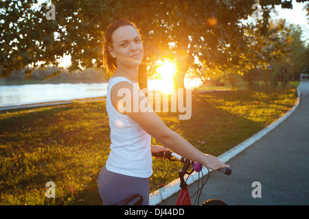 Giovane donna sorridente con la bicicletta nel parco Foto Stock