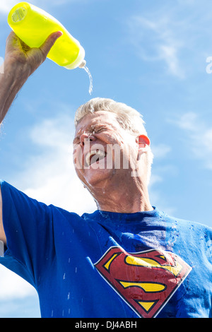 Uomo anziano, che indossa la maglietta di superman, versando acqua sul viso per alleviare l'esaurimento del calore, Stati Uniti Foto Stock