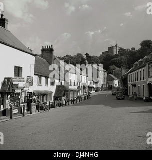 Historical, 1950s, Dunster High Street. Dunster è un antico villaggio risalente al Medioevo, con un antico castello - visto sullo sfondo - priorato, colombaia, mercato dei filati, locande e tearooms a Somerset, Inghilterra. Foto Stock