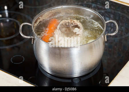 Far sobbollire la zuppa di pollo con il condimento di verdure nella pentola in acciaio sul vetro fornello ceramico Foto Stock