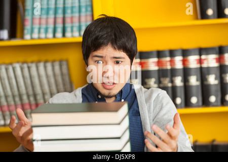 Studente guardando alla pila di libri della Biblioteca universitaria Foto Stock