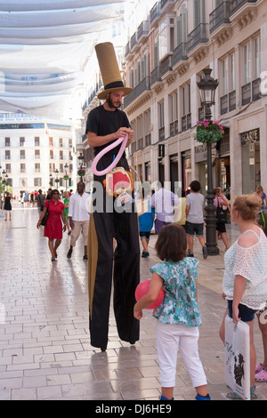 Stilt walking street performer rendendo palloncino giocattoli per bambini. Foto Stock