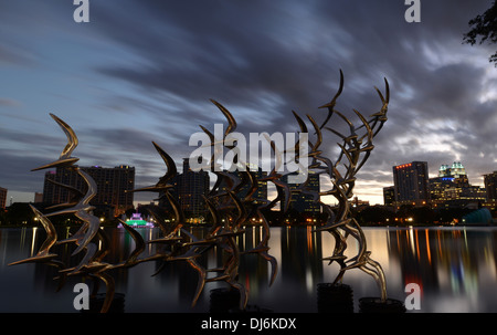Vedere Arte Scultura Orlando " prendere il volo' dall'artista Douwe Blumberg sul Lake Eola con il centro cittadino di Orlando, Florida edifici. Foto Stock