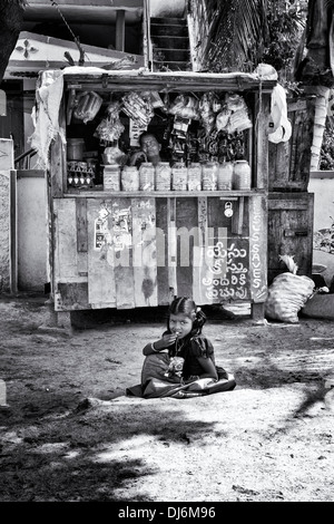 Ragazza indiana mangiando snack seduto di fronte un rurale villaggio indiano shop. Andhra Pradesh, India. In bianco e nero Foto Stock