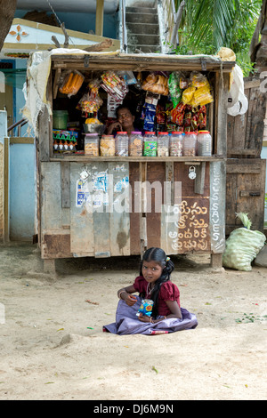 Ragazza indiana mangiando snack seduto di fronte un rurale villaggio indiano shop. Andhra Pradesh, India Foto Stock