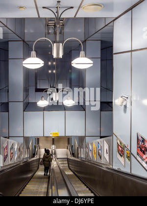 Donna discendente dei " commuters " sulla scala mobile al moderno DLR della metropolitana stazione ferroviaria, Londra Foto Stock