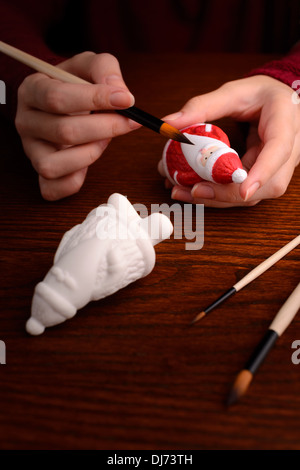 Le decorazioni di Natale: donna mani con porcellana statuetta di Santa, pittura, facendo della decorazione di Natale Foto Stock