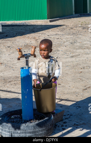 Sud Africa, Cape Town, Khayelitsha Township. Little Boy con benna a studiare la comunità il rubinetto dell'acqua. Foto Stock