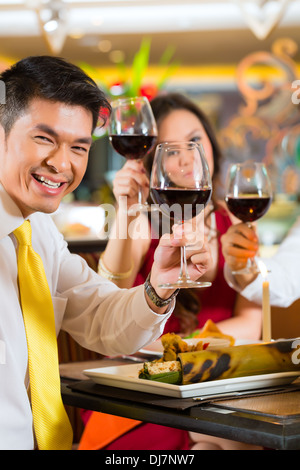 Due coppie o amici o persone di affari la tostatura mentre la cena o il pranzo in un ristorante elegante con vino rosso bicchieri Foto Stock