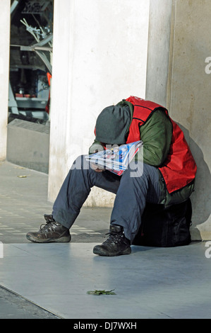 Grande problema venditore avvolto contro il freddo e addormentato al sole, Central London, England Regno Unito Foto Stock