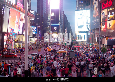 Una folla di persone si radunano sotto le insegne al neon in Times Square a New York City di notte. Foto Stock