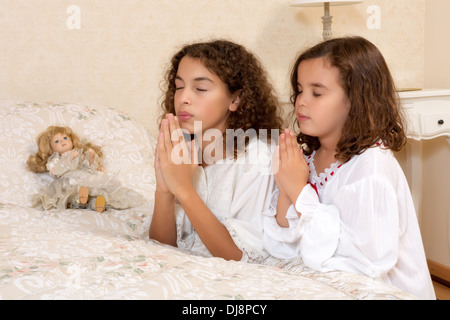 Adorabili ragazze vittoriane inginocchiato nella loro camera da letto vintage e la preghiera Foto Stock