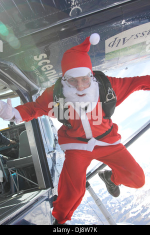 Questo paracadutista in un Babbo Natale costume è salta fuori di un aeromobile in un sit posizione sul cielo blu. Foto Stock