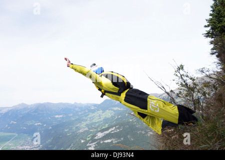 Uomo in tuta gialla sta uscendo dalla scogliera giù nella valle. Lui sta andando a cadere per 7 secondi prima di aprire il paracadute. Foto Stock