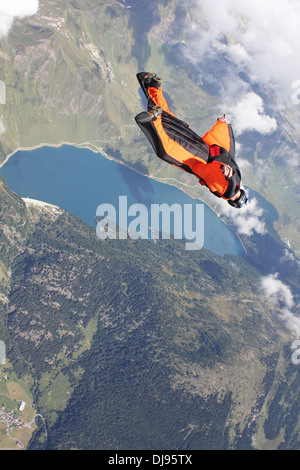 Uomo in tuta con Orange Wings è volare su un lago blu accanto alle nubi. Lui è molto felice per volare nel cielo blu. Foto Stock