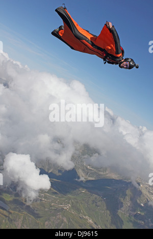 Uomo in tuta con Orange Wings è volare sopra le montagne accanto alle nubi. Lui è molto felice per volare nel cielo blu. Foto Stock