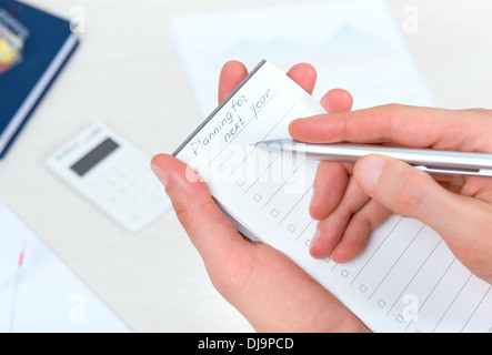 Persona d'affari di pensare e di scrivere una nuova pianificazione elenco di impegni in agenda per il prossimo anno con la penna a sfera in ufficio Foto Stock