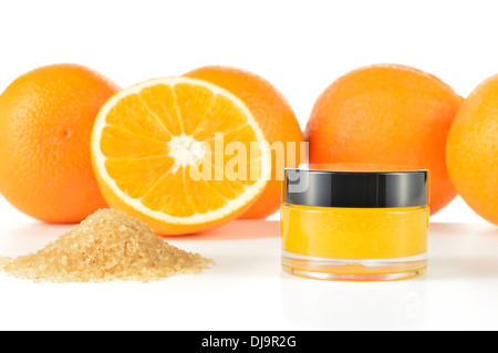 Arancio naturale di zucchero macchia a labbro su sfondo bianco con la riflessione. Cosmetici arancio in un vaso di vetro con le arance in uno sfondo. Foto Stock