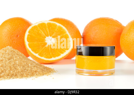 Arancio naturale di zucchero macchia a labbro su sfondo bianco con la riflessione. Cosmetici arancio in un vaso di vetro con le arance in uno sfondo. Foto Stock