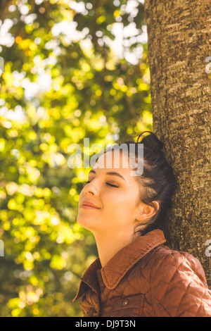 Vista laterale di brunette donna appoggiato a un albero Foto Stock