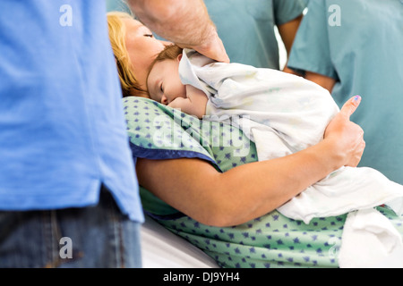 Babygirl giacente sulla madre circondata da infermieri e padre Foto Stock