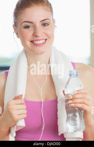 Donna con asciugamano attorno al collo tenendo la bottiglia di acqua in studio fitness Foto Stock