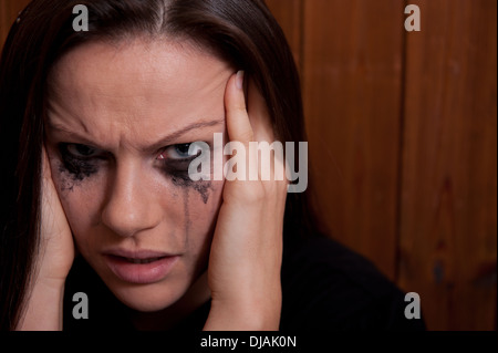 Giovane donna con il suo capo nelle sue mani e il suo make-up è in esecuzione da piangere. Foto Stock