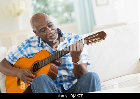 Uomo nero a suonare la chitarra sul divano Foto Stock