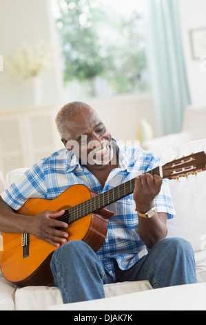 Uomo nero a suonare la chitarra sul divano Foto Stock
