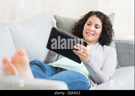 Donna ispanica con tavoletta digitale sul divano Foto Stock