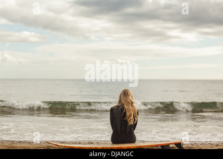 Vista posteriore del biondino di muta con la tavola da surf in spiaggia Foto Stock