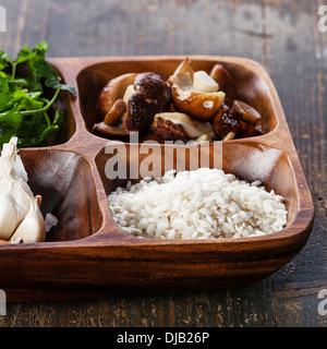 Bianco crudo riso nel recipiente di legno con ingredienti per il risotto con funghi selvatici Foto Stock