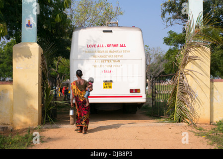 Donna indiana che porta il bambino a camminare verso lo Sri Sathya Sai Baba mobile ospedale outreach service bus. Andhra Pradesh, India Foto Stock