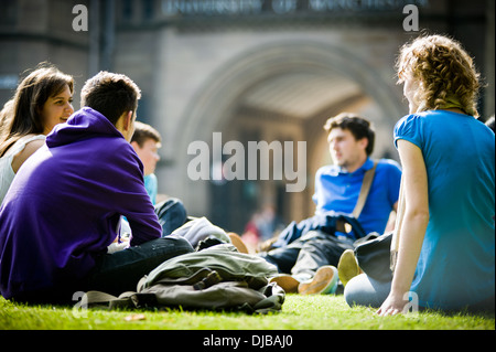 Gruppo di multi razziale Manchester studenti universitari sat sull'erba in campus sunshine parlando e ridendo cercando felice Foto Stock