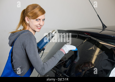 Lavoratore di sesso femminile che di colorazione del vetro per auto in garage con una lamina oscurata o film Foto Stock