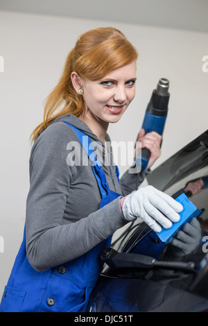 Lavoratore di sesso femminile che di colorazione del vetro per auto in garage con una lamina oscurata o film Foto Stock