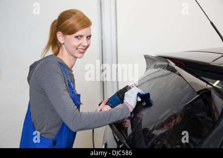 Lavoratore di sesso femminile che di colorazione del vetro per auto in garage con una lamina oscurata o film Foto Stock