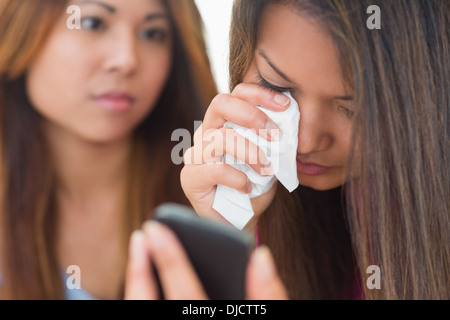 Il pianto della donna guardando il telefono è confortato dalla sua sorella Foto Stock