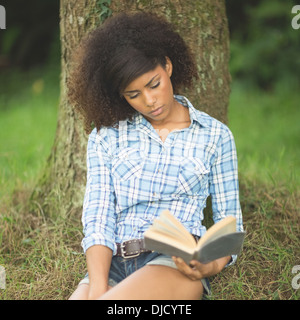 Gravi Gorgeous Brunette appoggiata contro la lettura dell'albero Foto Stock