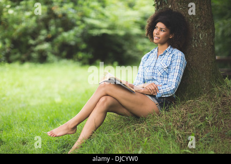 Contenuto Gorgeous Brunette appoggiata contro la lettura dell'albero Foto Stock