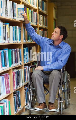 Calma uomo in carrozzella assumendo un libro a scaffale Foto Stock