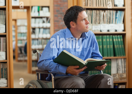 Malinconici uomo in sedia a rotelle in possesso di un libro Foto Stock