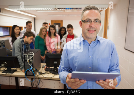 Insegnante di informatica in piedi nella parte anteriore della sua classe utilizzando un tablet Foto Stock