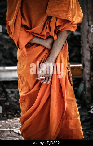 Monaco tailandese che fuma e nasconde una sigaretta dietro la schiena. Thailandia S. E. Asia Monk da dietro Foto Stock