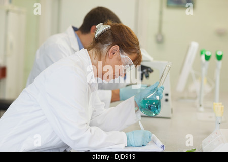 Donna scienziato appoggiato su una scrivania la scrittura su una clipboard Foto Stock